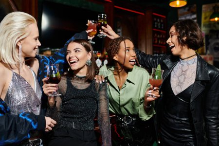 Unbekümmerte multirassische Freundinnen, die Cocktailgläser in der modernen Bar klirren, Glück und Freizeit