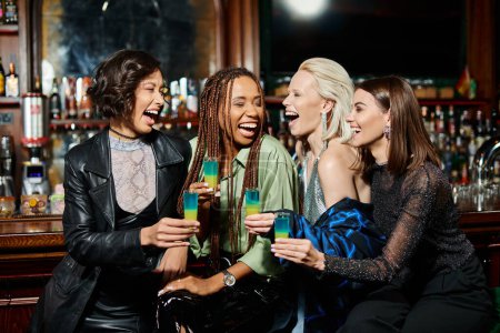 Photo for Excited multiracial female friends with shot glasses laughing in modern bar, party time - Royalty Free Image