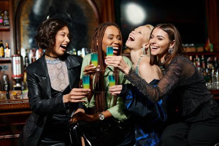 Photo for Overjoyed and trendy multiracial girlfriends with shot glasses laughing in modern bar, hen party - Royalty Free Image