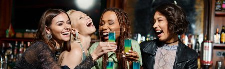 Photo for Cheerful and stylish multiracial girlfriends with shot glasses laughing in modern bar, banner - Royalty Free Image