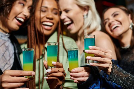 Photo for Selective focus of shot glasses near cheerful multiethnic girlfriends on blurred background - Royalty Free Image