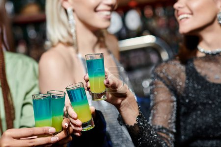 Photo for Cropped view of blurred multiracial female friends clinking shot glasses in modern bar, party - Royalty Free Image