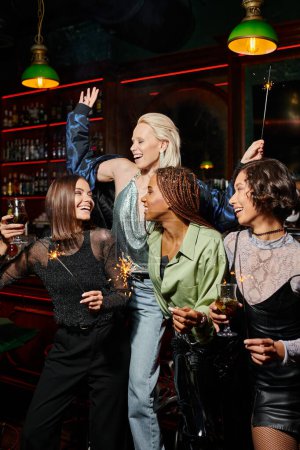 novias multiétnicas llenas de alegría con cócteles y brillantes chispas que se divierten en el bar, tiempo de fiesta