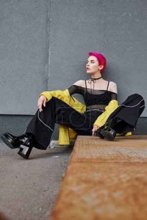 young fashionable woman in urban trendy clothes sitting and posing on street, fashion concept