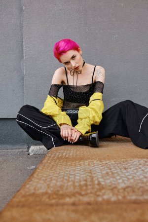 young appealing woman with short pink hair and tattoos sitting and looking at camera, fashion