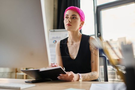 young attractive businesswoman with pink hair and tattoos in urban casual outfit looking at computer