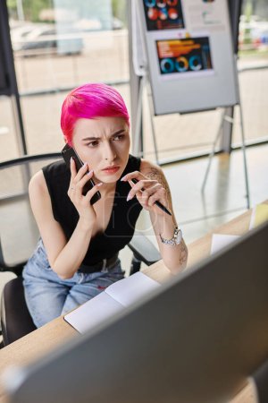 Téléchargez les photos : Jeune femme concentrée avec stylo à la main parlant par téléphone et regardant l'ordinateur, concept d'entreprise - en image libre de droit