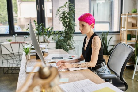 attractive businesswoman with tattoos and pink hair in casual attire working at her computer