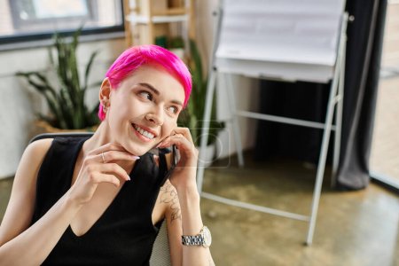 joyous pink haired woman with tattoos talking by phone while working hard, business concept