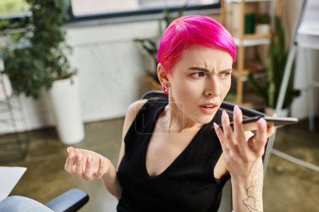 irritated pretty businesswoman with tattoos and pink hair talking unhappily by phone at office