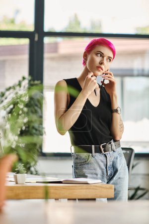 Téléchargez les photos : Jeune travailleuse attentive aux cheveux courts roses parlant par téléphone au bureau, concept d'entreprise - en image libre de droit