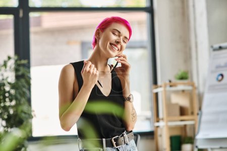 Téléchargez les photos : Joyeuse jeune femme d'affaires avec des tatouages parlant par téléphone et souriant joyeusement avec les yeux fermés - en image libre de droit