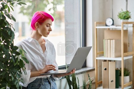 hermosa mujer de negocios de pelo rosa en camisa blanca y jeans trabajando en su computadora portátil mientras está de pie