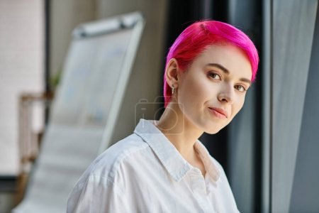 joven mujer de negocios de pelo rosa con pendiente de camisa blanca posando y mirando directamente a la cámara