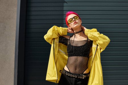 rosafarbene junge Frau mit gelber Sonnenbrille und trendigem Outfit posiert im Freien, Streetstyle-Mode