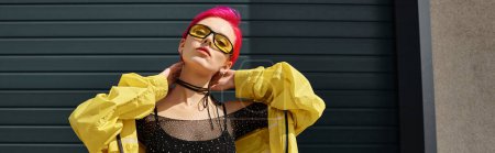 Foto de Mujer joven de pelo rosa en gafas de sol amarillas y traje de moda posando al aire libre, pancarta - Imagen libre de derechos