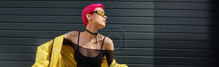 Foto de Mujer atractiva con el pelo rosa y tatuaje posando en gafas de sol y ropa de calle de moda, pancarta - Imagen libre de derechos