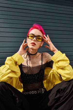 Foto de Elegante mujer elegante con pelo rosa y tatuaje posando en gafas de sol y ropa de calle de moda en la calle - Imagen libre de derechos