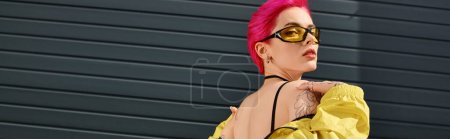 Foto de Mujer joven de pelo rosa en gafas de sol amarillas y traje de moda posando y mirando a la cámara, pancarta - Imagen libre de derechos