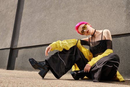 Foto de Longitud completa, chica de pelo rosa en gafas de sol amarillas y traje de moda posando y mirando a la cámara - Imagen libre de derechos