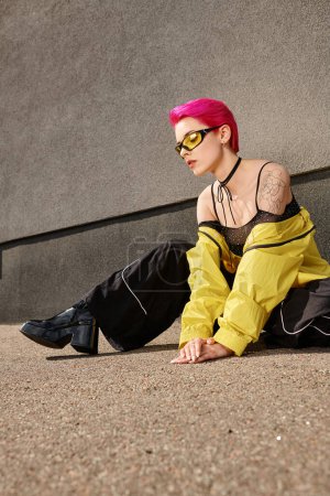 Foto de Larga duración, mujer de pelo rosa en gafas de sol amarillas y traje de moda posando en la calle. mirada elegante - Imagen libre de derechos
