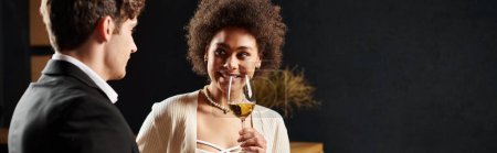 femme afro-américaine tenant un verre de vin et regardant l'homme pendant la date le jour de la Saint-Valentin, bannière