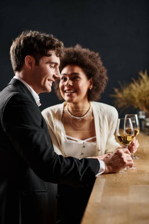 freudige afrikanisch-amerikanische Frau hält ein Weinglas in der Hand und schaut den Mann beim Date am Valentinstag an