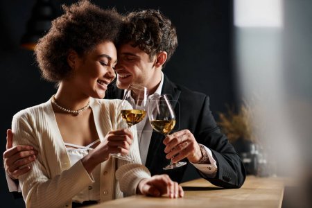 feliz pareja interracial tintineo vasos de vino blanco durante la fecha en el día de San Valentín, romance