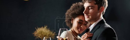 happy man holding glass of wine and hugging curly african american girlfriend during date, banner