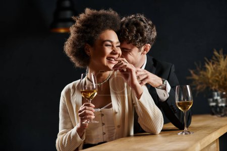 glückliches multikulturelles Paar lacht, während es beim Date mit Weingläsern am Tresen sitzt