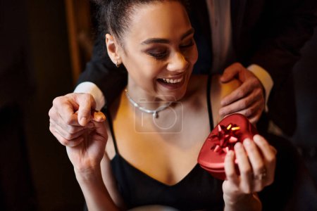 hombre de la mano de la mujer afroamericana feliz después de regalar la caja en forma de corazón en el día de San Valentín