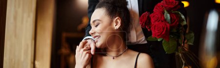Téléchargez les photos : Homme tenant des roses rouges près heureuse femme afro-américaine sur la Saint-Valentin, bannière horizontale - en image libre de droit