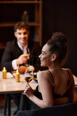 happy african american woman holding glass of wine during date with man on Saint Valentines day