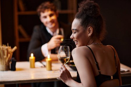 fröhliche afrikanisch-amerikanische Frau beim Date mit einem Mann am Valentinstag mit einem Glas Wein