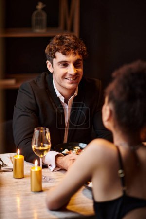 Photo for Joyful man in elegant attire looking at girlfriend on blurred foreground during date in restaurant - Royalty Free Image