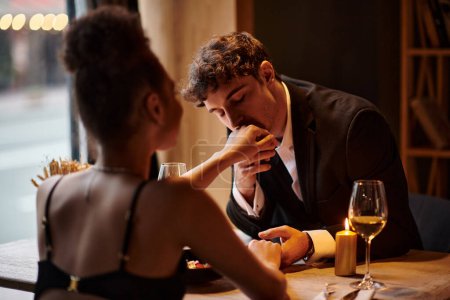 Gentleman in eleganter Kleidung küsst die Hand seiner Freundin beim Date im Restaurant, Valentinstag