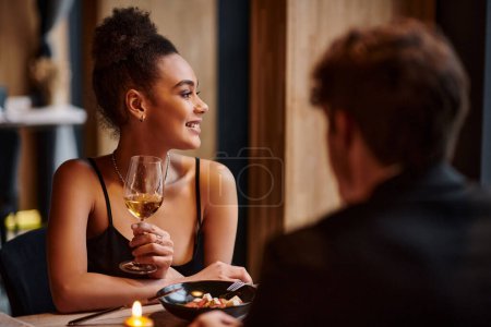 Photo for Happy african american woman holding wine glass next to boyfriend during date on Valentines day - Royalty Free Image