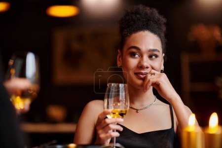 fröhliche afrikanisch-amerikanische Frau lächelnd und mit einem Glas Wein beim Date am Valentinstag