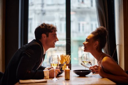 fröhliche afrikanisch-amerikanische Frau lächelt und sieht Mann beim Dinner-Date am Valentinstag an