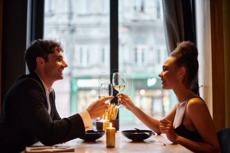 cheerful african american woman clinking glasses of wine with man during date on Valentines day
