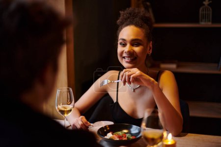 Photo for Happy african american woman enjoying salad during date with boyfriend in restaurant, Valentines day - Royalty Free Image