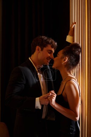 Photo for Happy man in formal wear seducing pleased and beautiful african american woman in black dress - Royalty Free Image