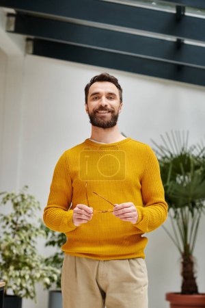 joyful handsome architect with glasses in yellow turtleneck posing in his office during work