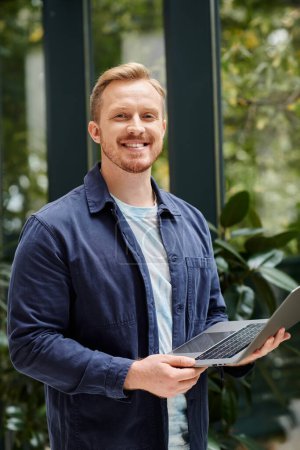 joyous good looking architect in everyday clothes holding his laptop and working on his startup