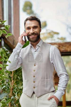attractive concentrated leader with beard in sophisticated attire talking by phone, business concept