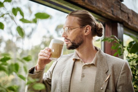 hombre atractivo de buen aspecto con barba y pelo recogido en traje elegante bebiendo su café caliente