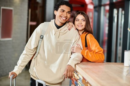 Alegre pareja interracial sonriendo en el mostrador de recepción del albergue, aparentemente emocionado por su viaje