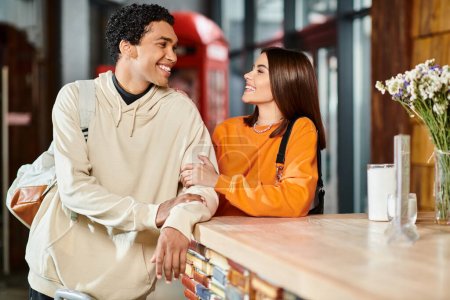 Feliz hombre negro y mujer disfrutando de una conversación mientras está de pie en el mostrador de recepción en el albergue