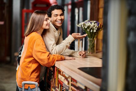 happy young woman smiling near her black boyfriend at hostel reception desk during check in