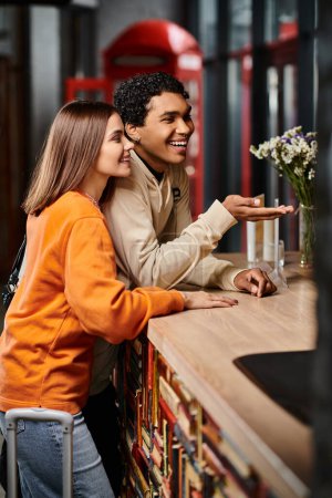 happy black man gesturing at reception desk in hostel, standing with cheerful young girlfriend